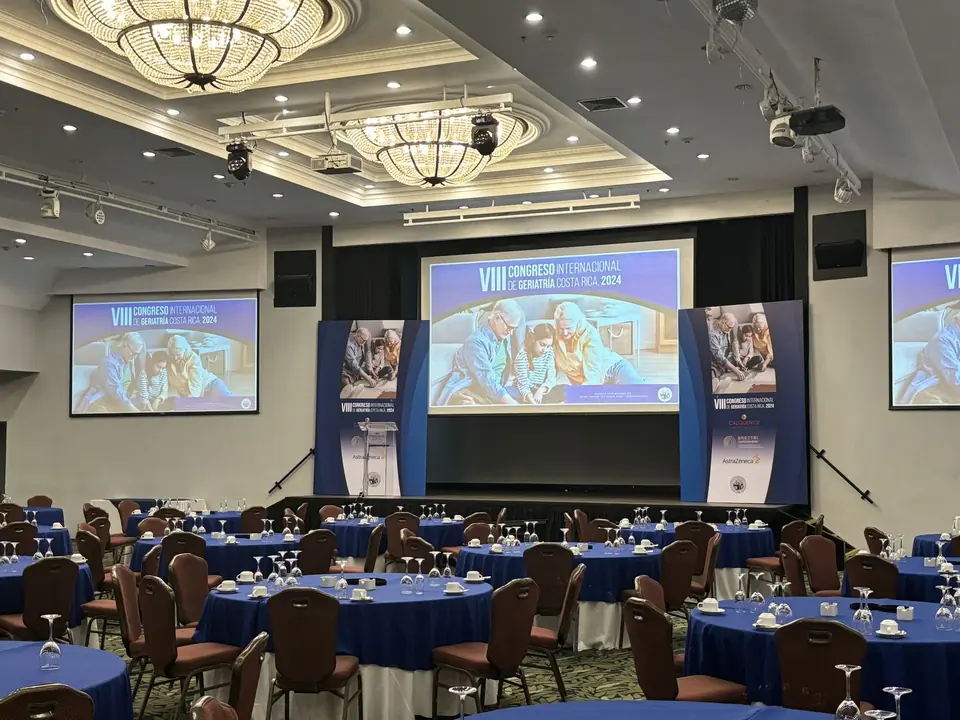 Sala plenaria de un congreso con escenario, marco de pantalla y mesas de banquete