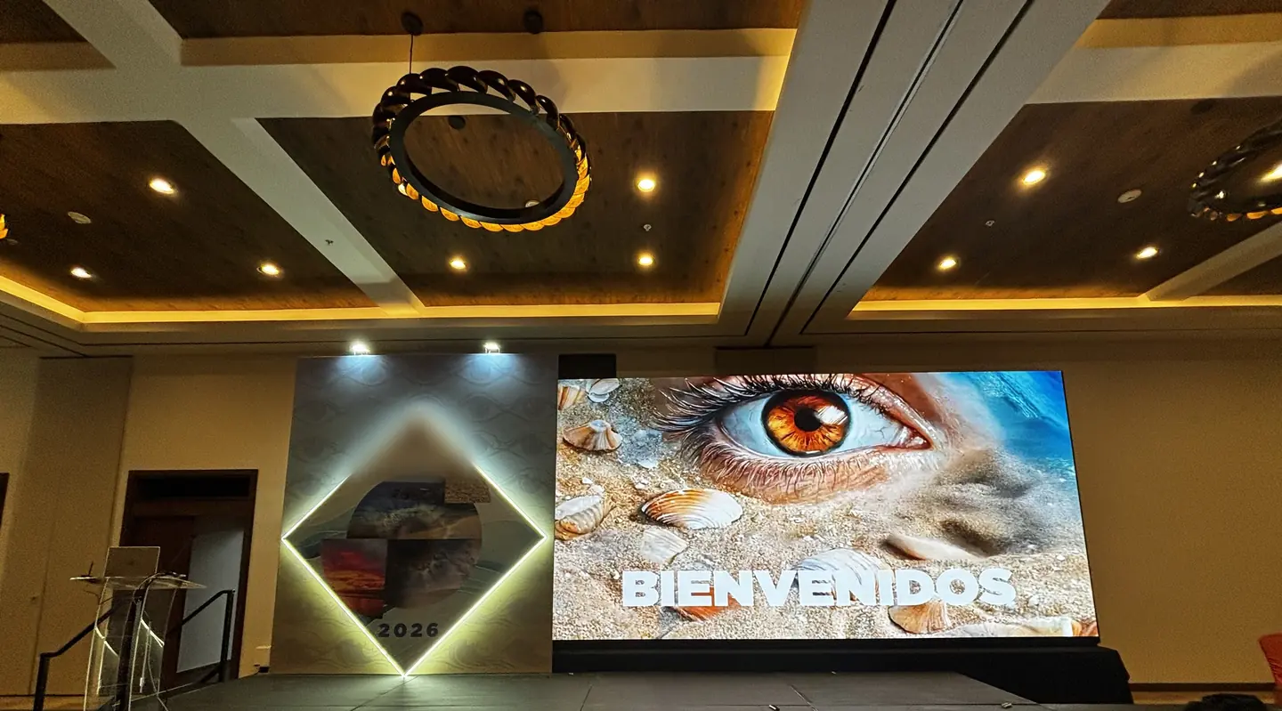 Escenario de congreso con una pantalla de bienvenida de gran formato y un rombo retroiluminado en un salón de hotel