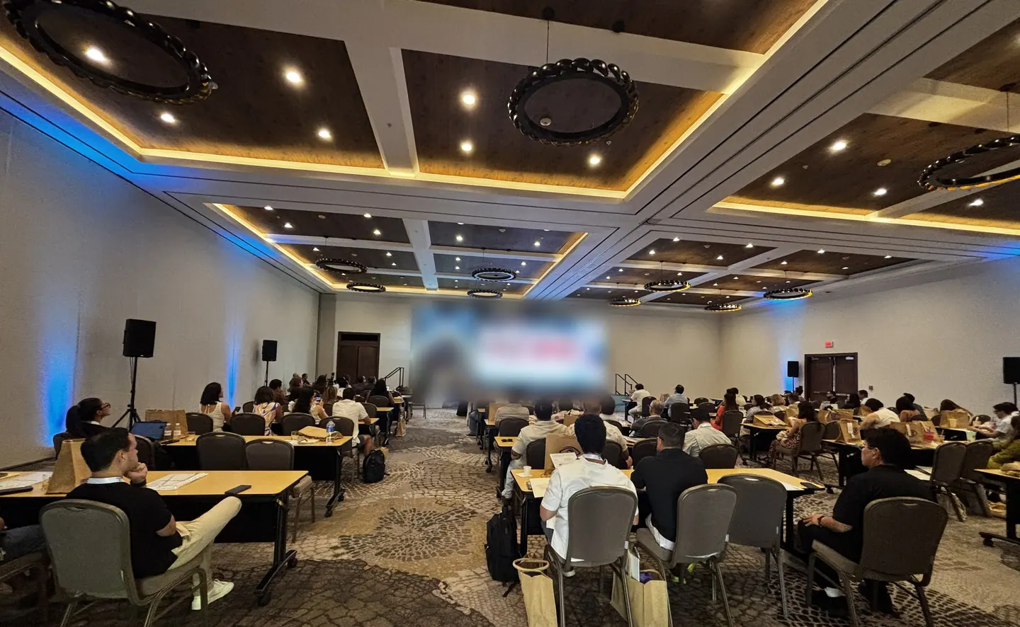 Sala de congreso en plena sesión, con asistentes en mesas de trabajo y el escenario al fondo