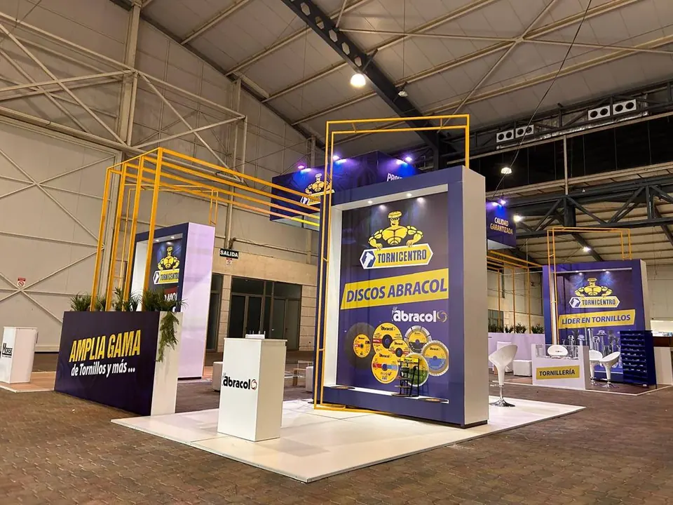 Stand de Tornicentro y Discos Abracol en feria industrial, con pórtico metálico amarillo y paneles azules de gran formato